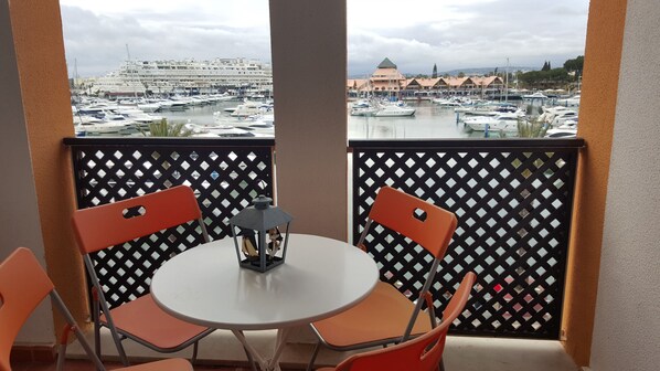 Ein Balkon mit Tisch und Stühlen, der auf einen Yachthafen mit Booten und Gebäuden blickt.