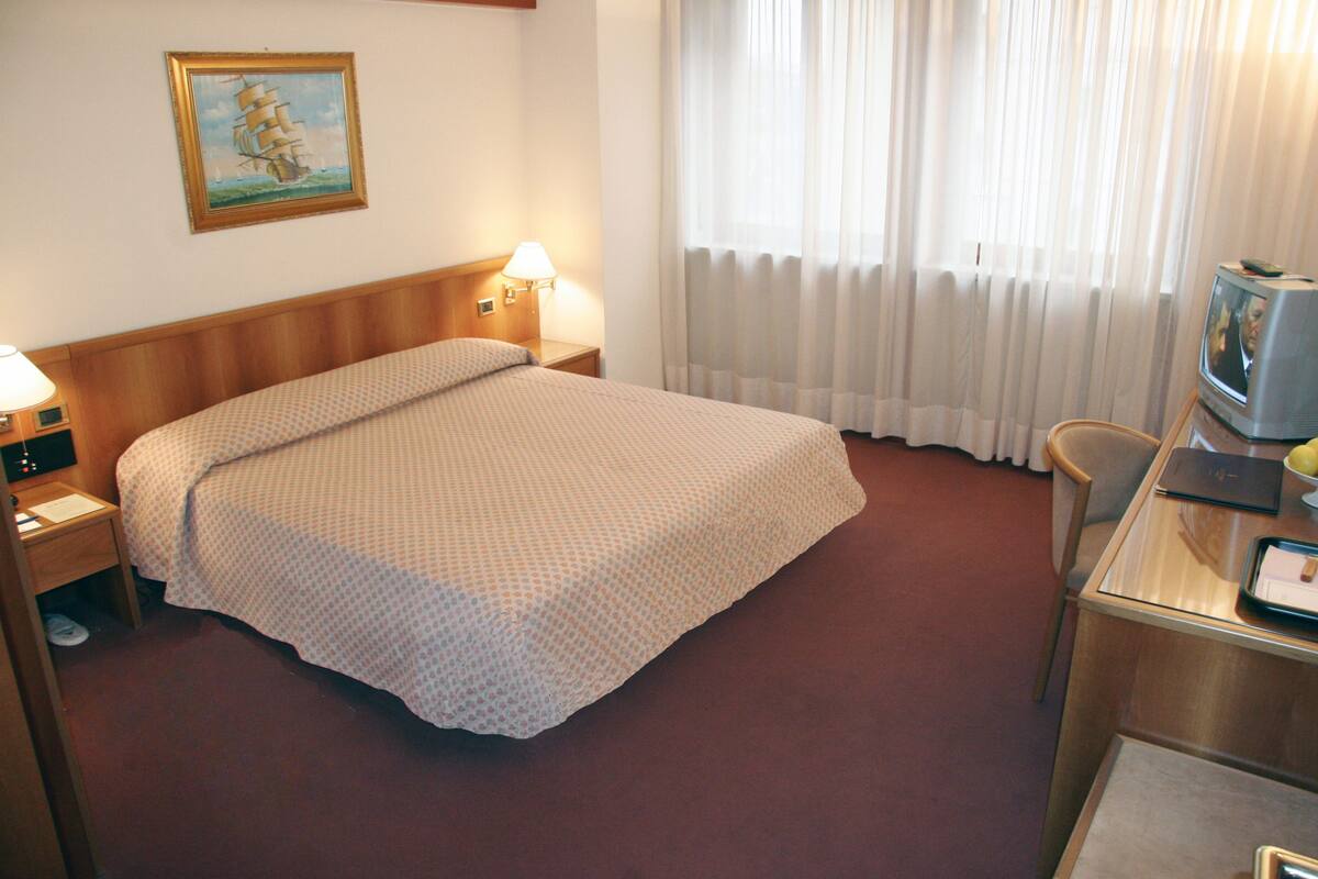 A hotel room with a large bed, a desk with a television, and a chair.