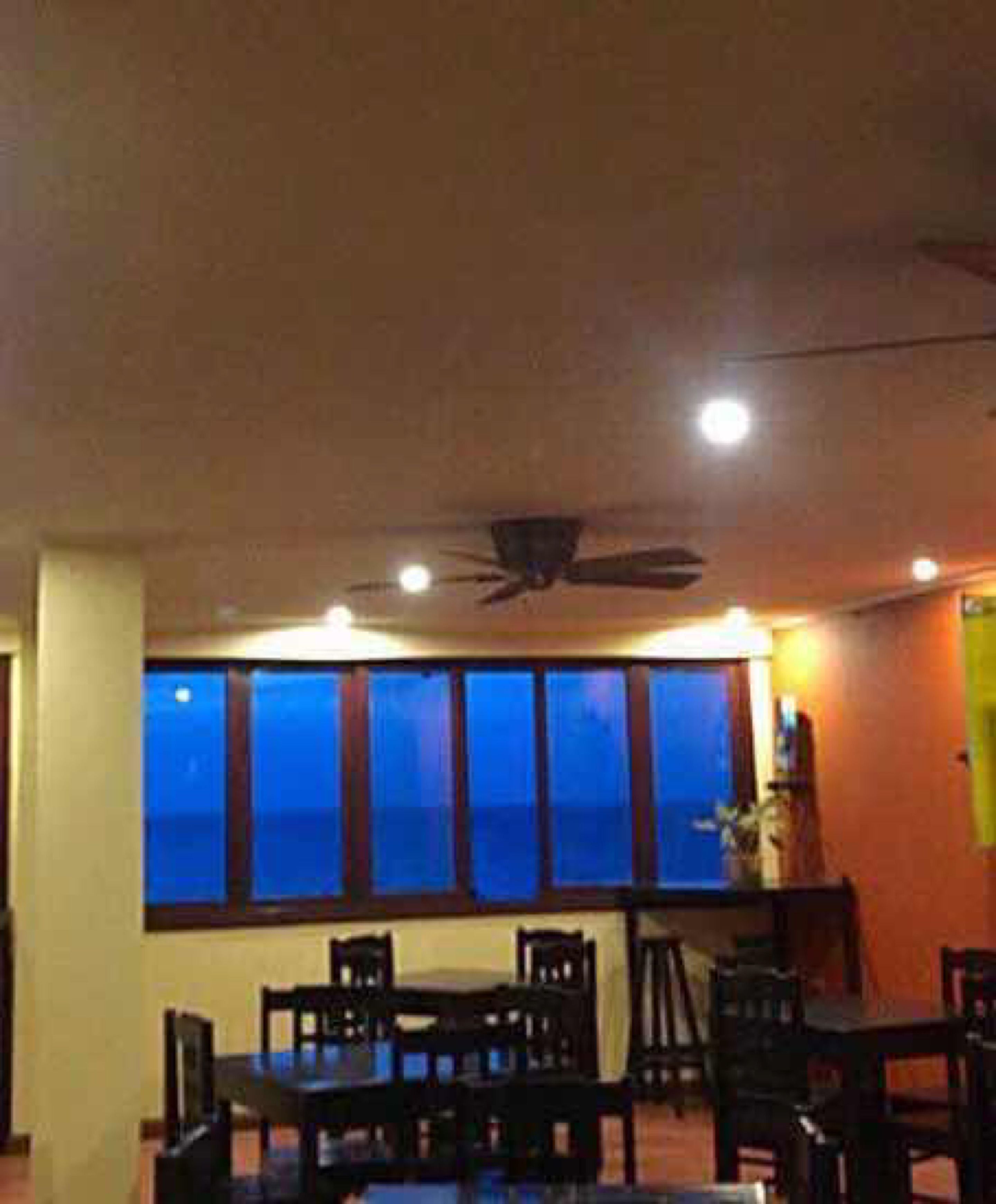 A dining area with a high ceiling, a ceiling fan, and large windows with a view.