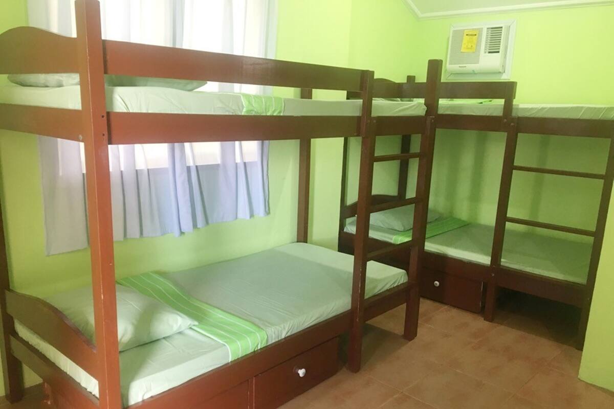 A bunk bed room with a window, curtains, and an air conditioning unit.
