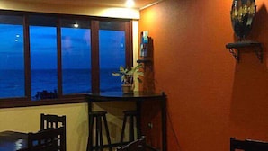 Un comedor con vista al océano, una mesa, sillas y un adorno en la pared.