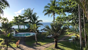 Zona de piscina con vista al océano, rodeada de palmeras y un sendero de piedra.