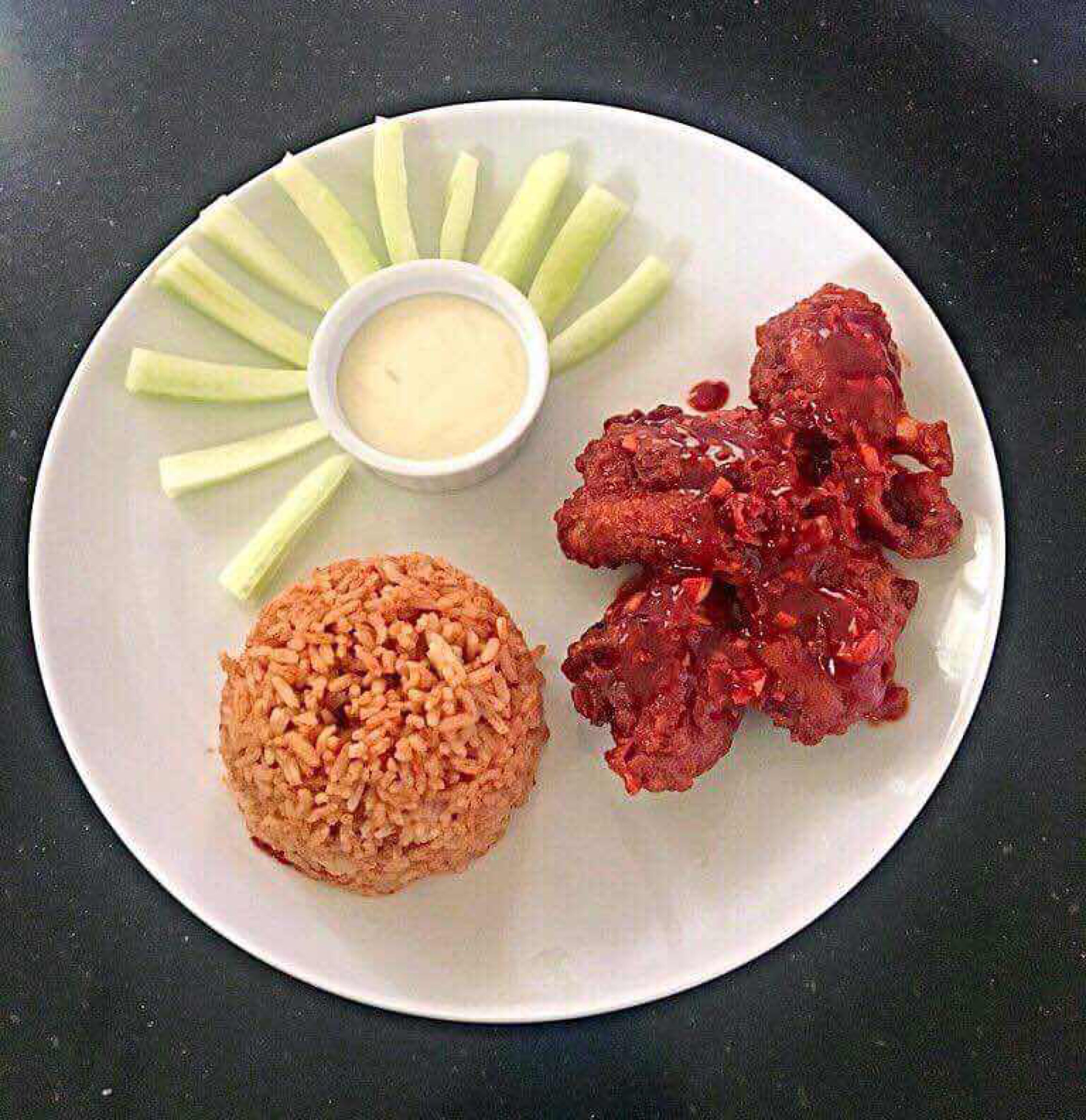 A plate with fried chicken, a mound of rice, and a small bowl of sauce, accompanied by celery sticks.
