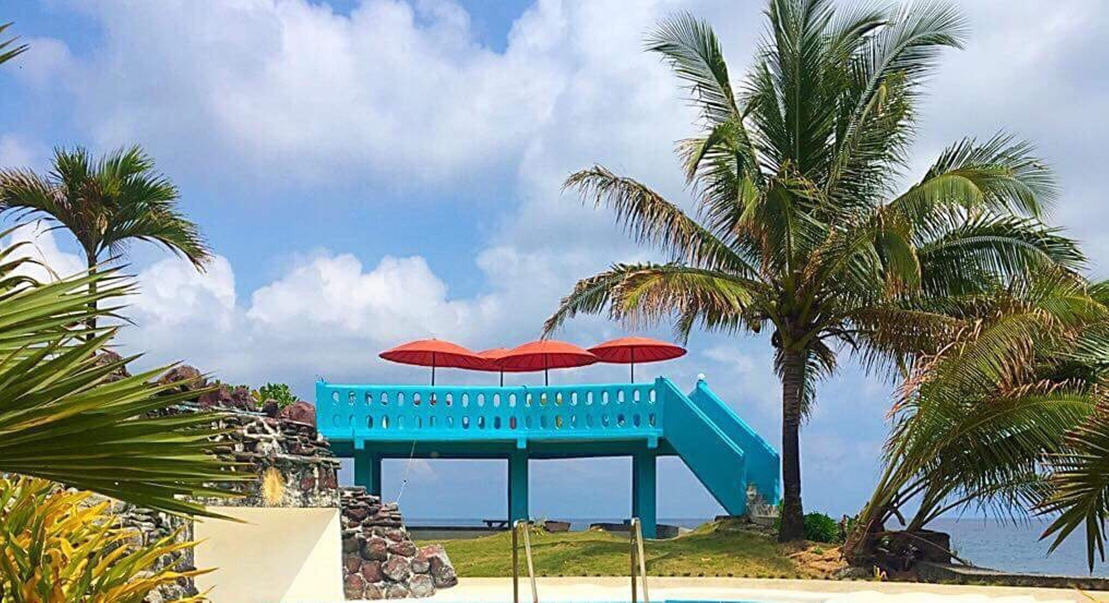 Uma escadaria azul-turquesa que leva a uma área de praia com guarda-sóis vermelhos.
