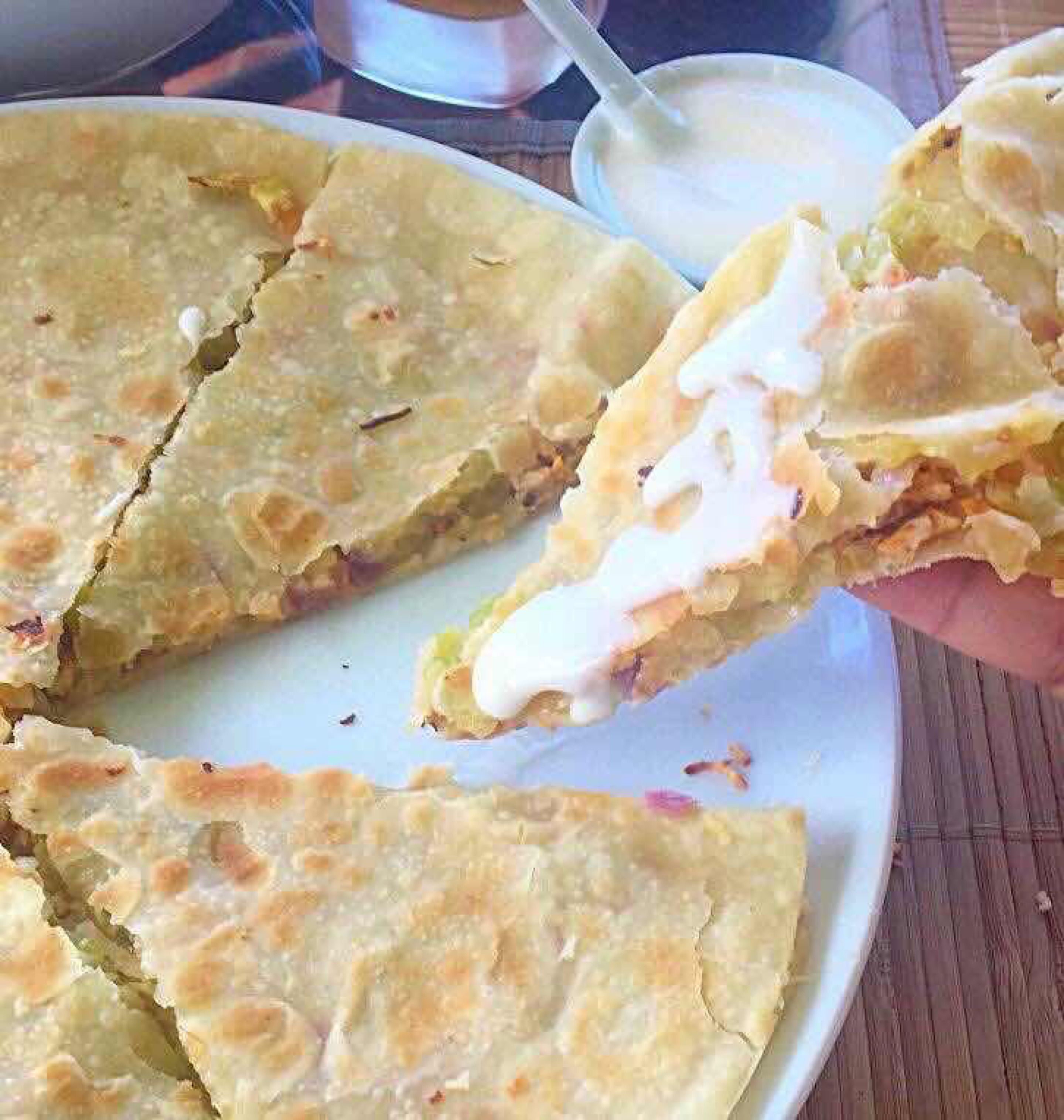 Een bord quesadilla's, in plakjes gesneden, waarvan er één omhooggehouden wordt.