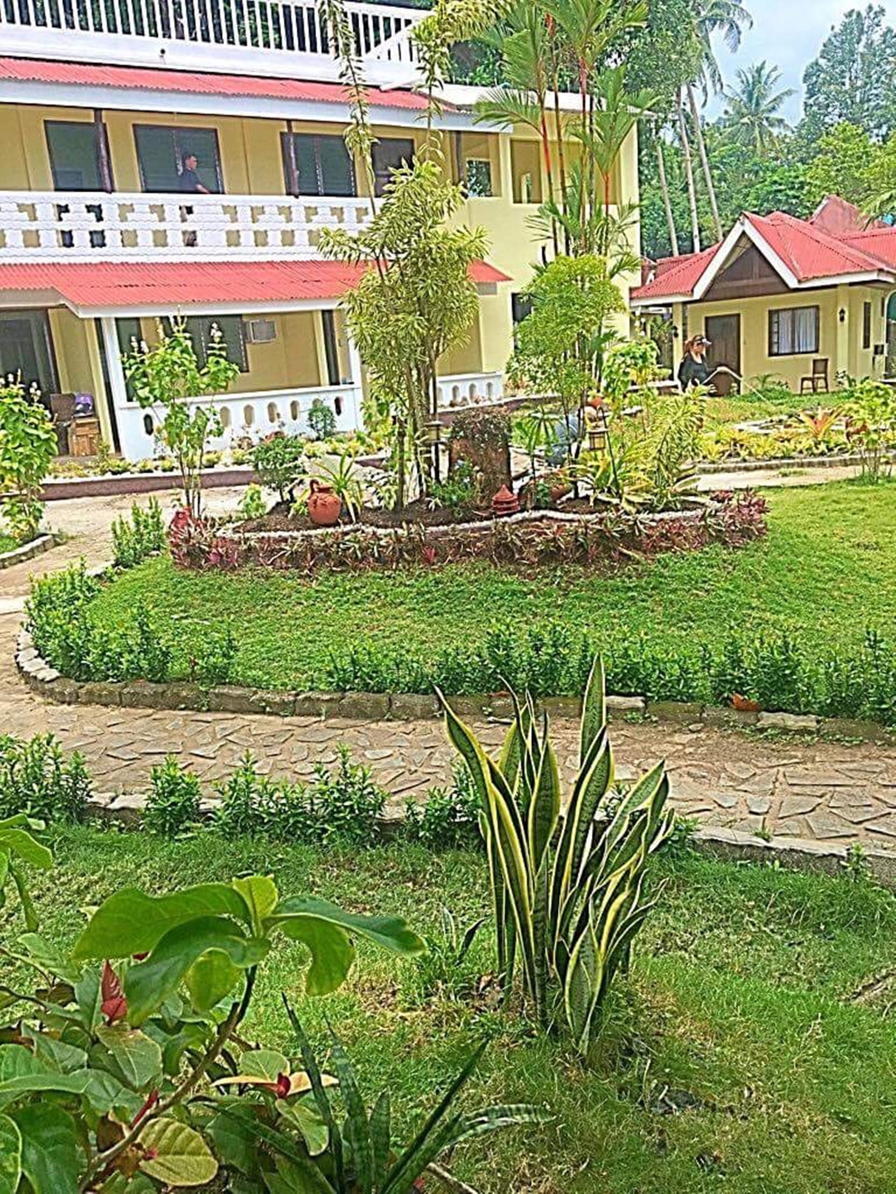 Un hotel con un jardín cuidado, senderos pavimentados y una gran variedad de plantas.