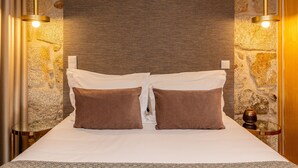 A neatly made bed with two pillows, a textured wall behind, and two pendant lights.