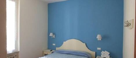 A bedroom with a bed, a ceiling fan, bedside lamps, and a window.