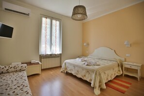 Un dormitorio con cama, mesitas de noche, televisor y ventana con cortinas.