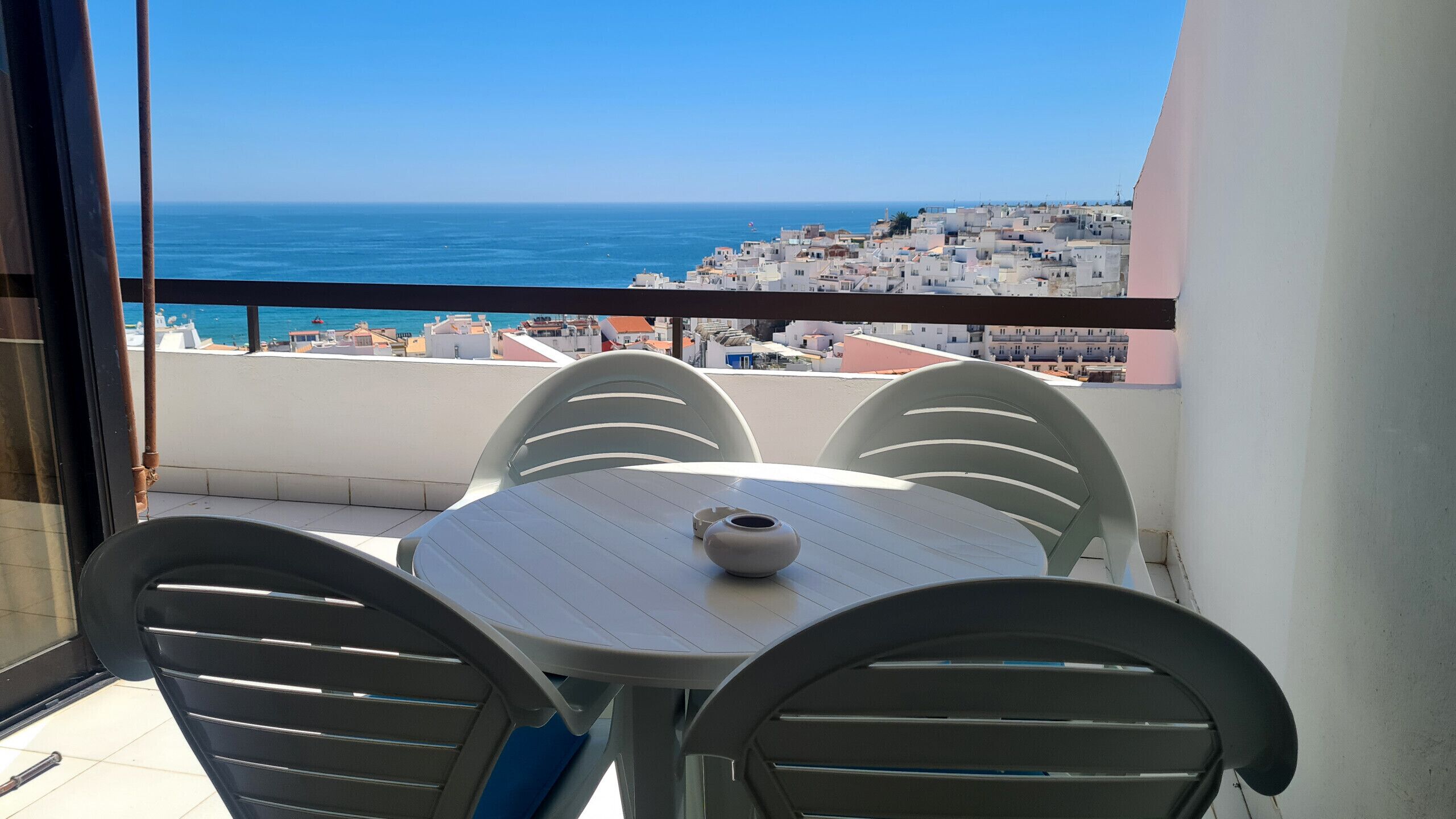 Un balcone con tavolo e sedie, con vista su una cittadina costiera e il mare.
