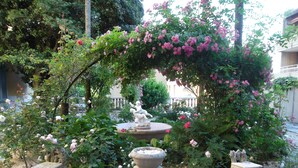 A garden with a stone fountain, a statue, and a pergola covered in pink flowers. - FeWo Luino Loft: Historic Charm, 100m to Lake & Swiss Gateway. (Luino)