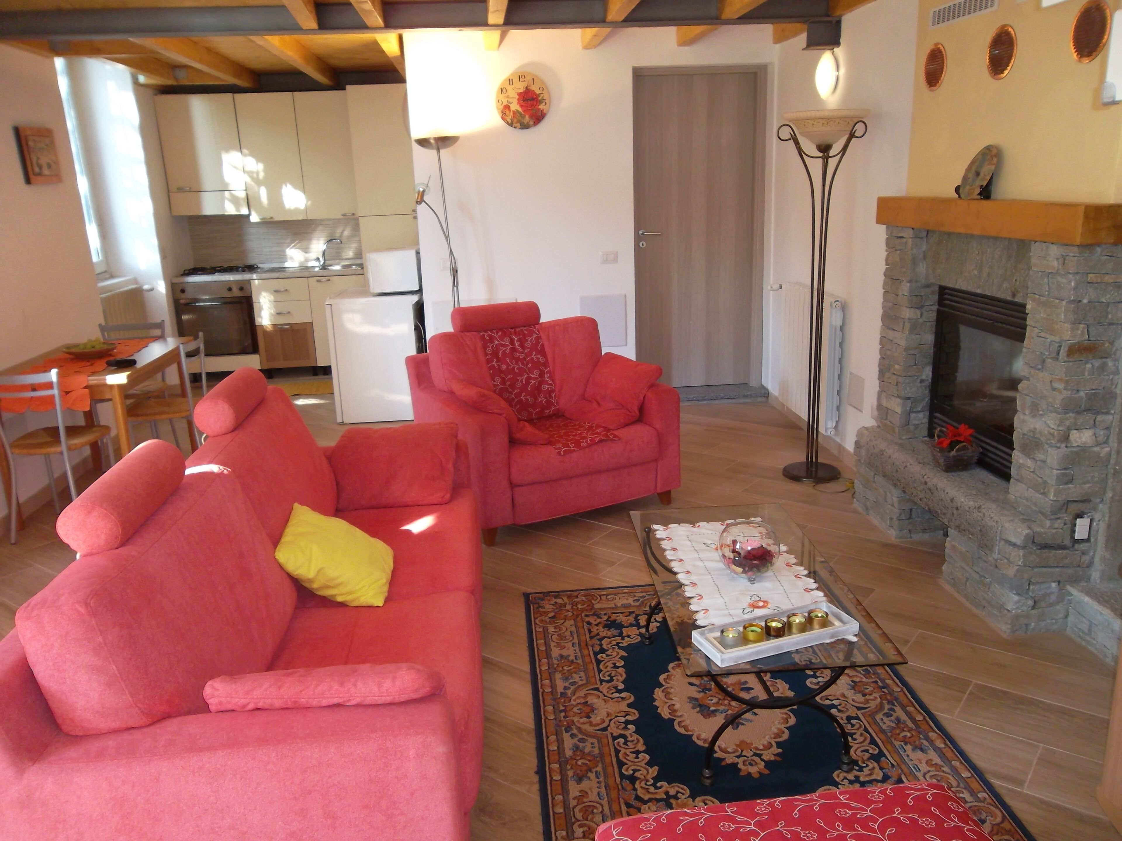 A living room with two red sofas, a coffee table with decorative items, a fireplace, and a kitchen in the background.