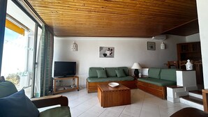 A living room with a green sofa, a wooden coffee table, a TV on a stand, and a balcony with a view. - Albufeira, Ocean terrace (22) (Albufeira)