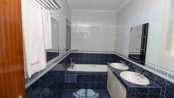 Un baño con dos lavamanos, una bañera y un espejo grande.
