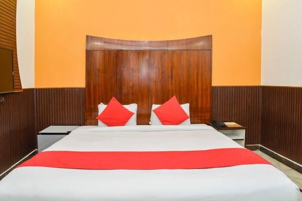 Une chambre d’hôtel avec une tête de lit en bois, un lit avec une literie blanche et rouge, et une table de chevet avec un téléphone.