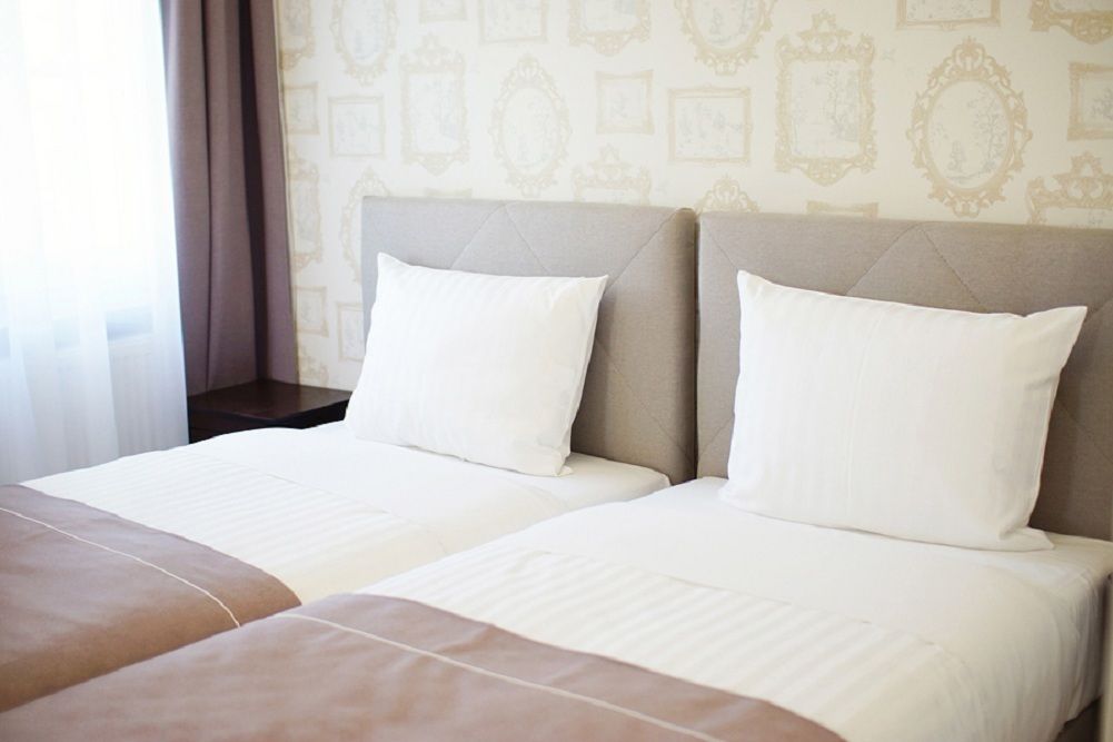 A hotel room with two beds, a beige headboard, and a patterned wallpaper.