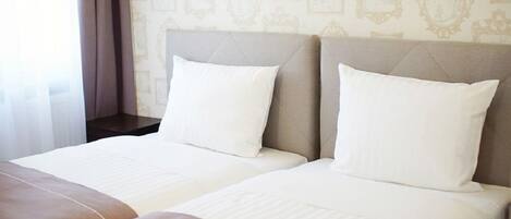 A hotel room with two beds, a beige headboard, and a patterned wallpaper.