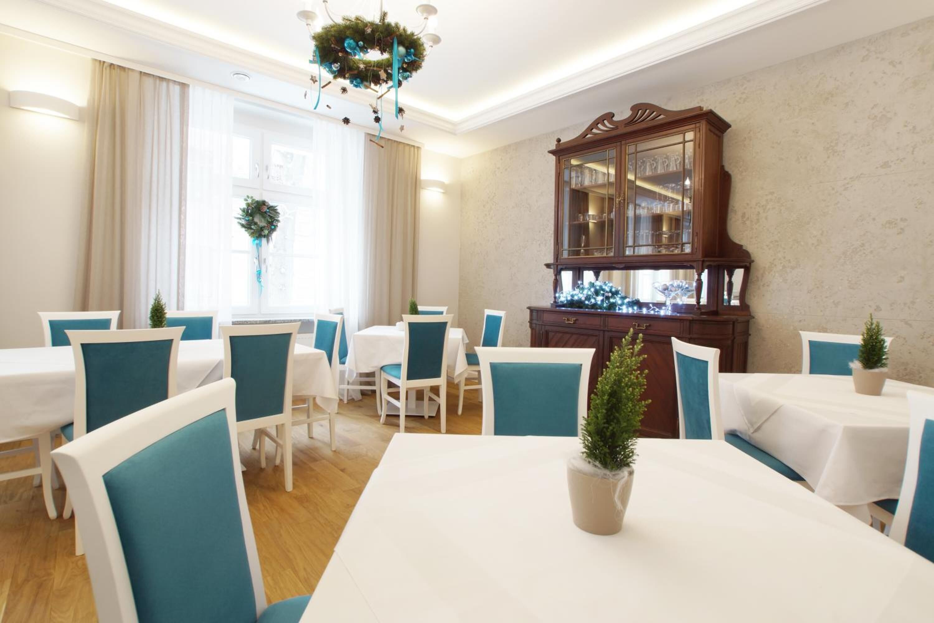 A dining area with white tables and teal chairs, a wooden cabinet, and a chandelier.