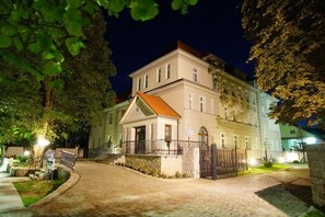 Un bâtiment à l’architecture traditionnelle, bien éclairé et à deux étages, doté d’une entrée imposante, d’une allée menant à un portail et d’un petit porche.