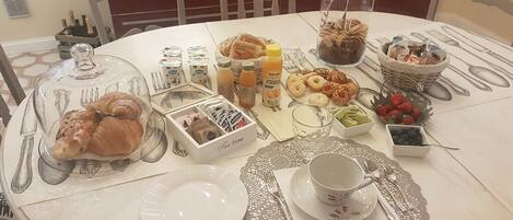 Una mesa de desayuno dispuesta con pasteles, frutas y bebidas, incluyendo un vaso de zumo de naranja y una botella de leche de soja.