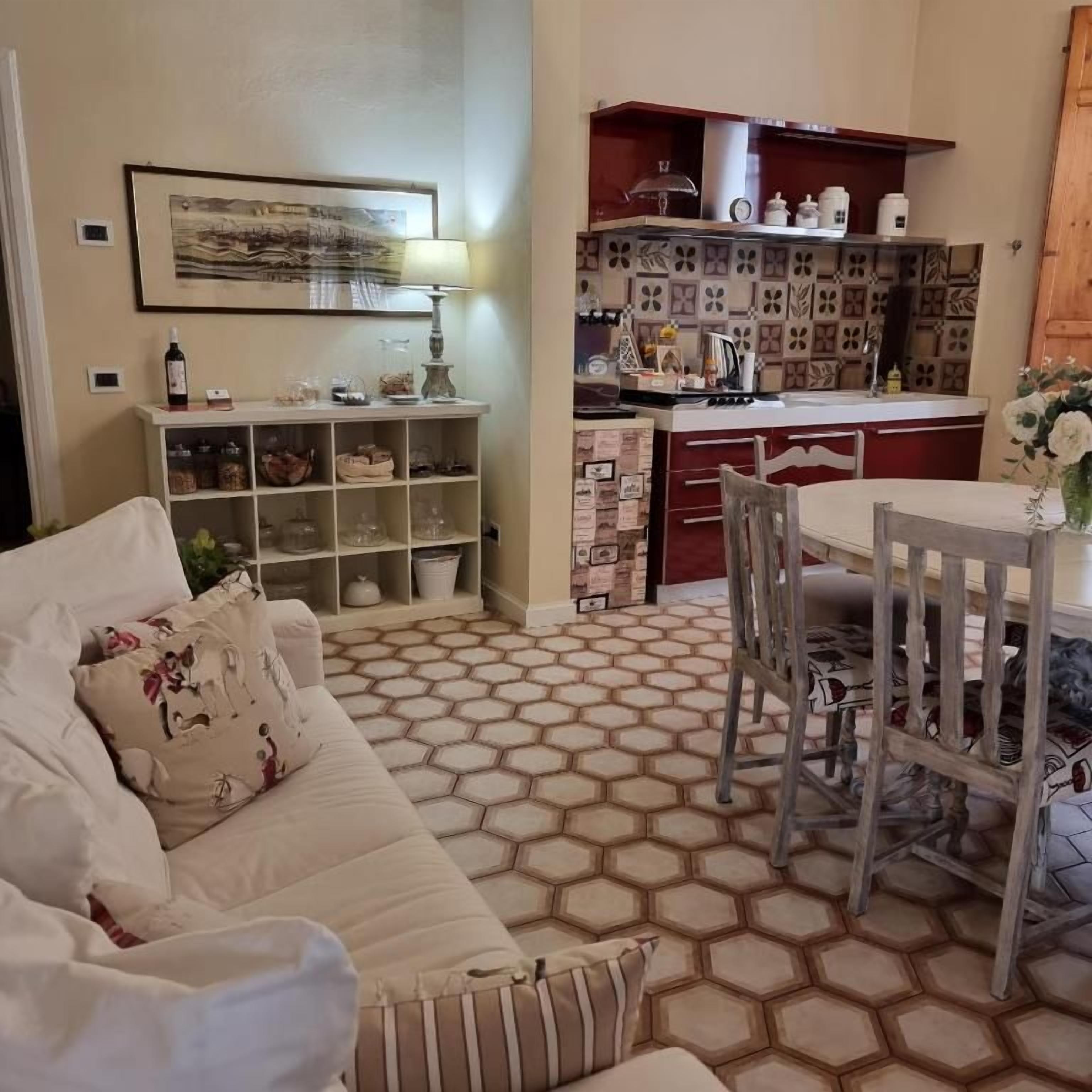 Una sala de estar con sofá, una mesa de comedor con sillas, una zona de cocina con armarios y un suelo estampado.