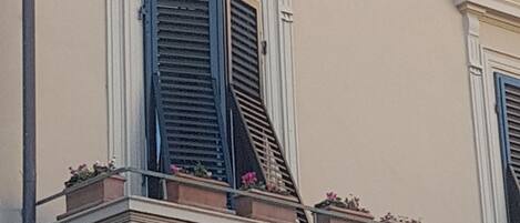 Un bâtiment doté d’un balcon orné d’une balustrade, d’une fenêtre avec des volets bleus et d’une porte donnant sur un petit balcon.