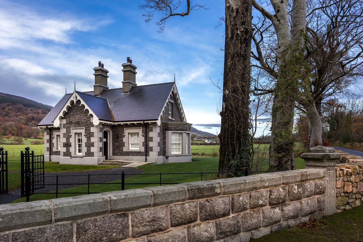 A stone house with a slate roof, a chimney, and a stone wall in the foreground.