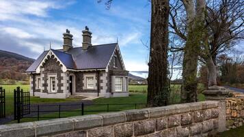 A stone house with a slate roof, a chimney, and a stone wall in the foreground.