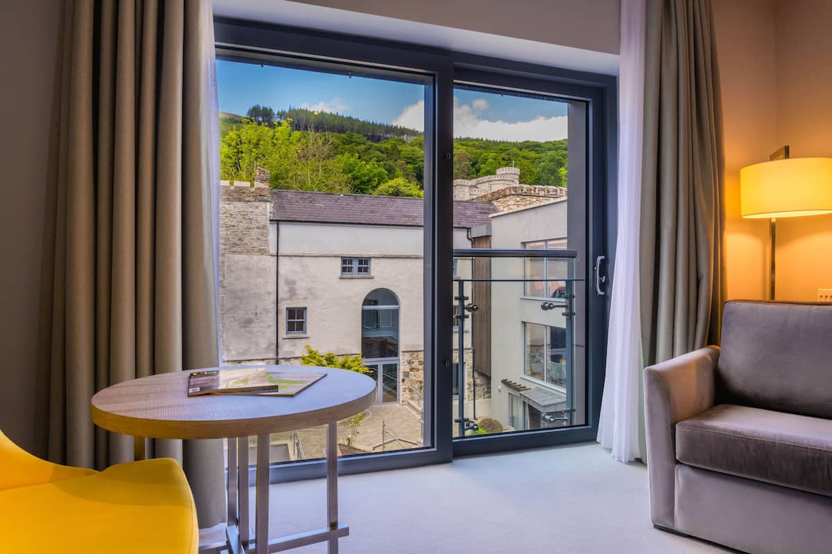 A room with a view of a hillside, a sofa, a table with a book, and a lamp.