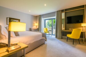 A hotel room with a bed, bedside table, lamp, chair, desk, TV, and a balcony with a view.
