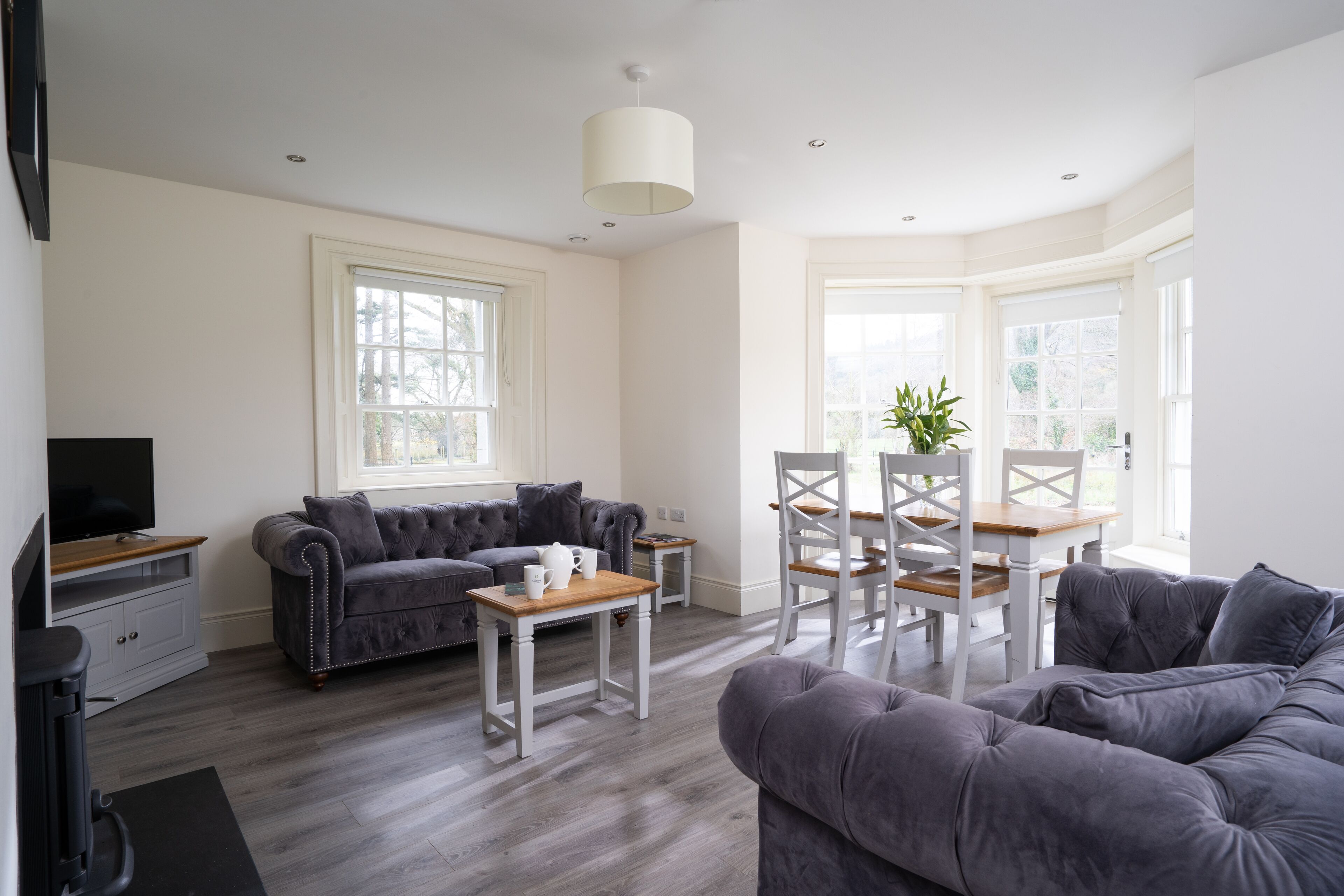 A modern living room with a grey sofa, a coffee table, and a dining area with white chairs and a wooden table.
