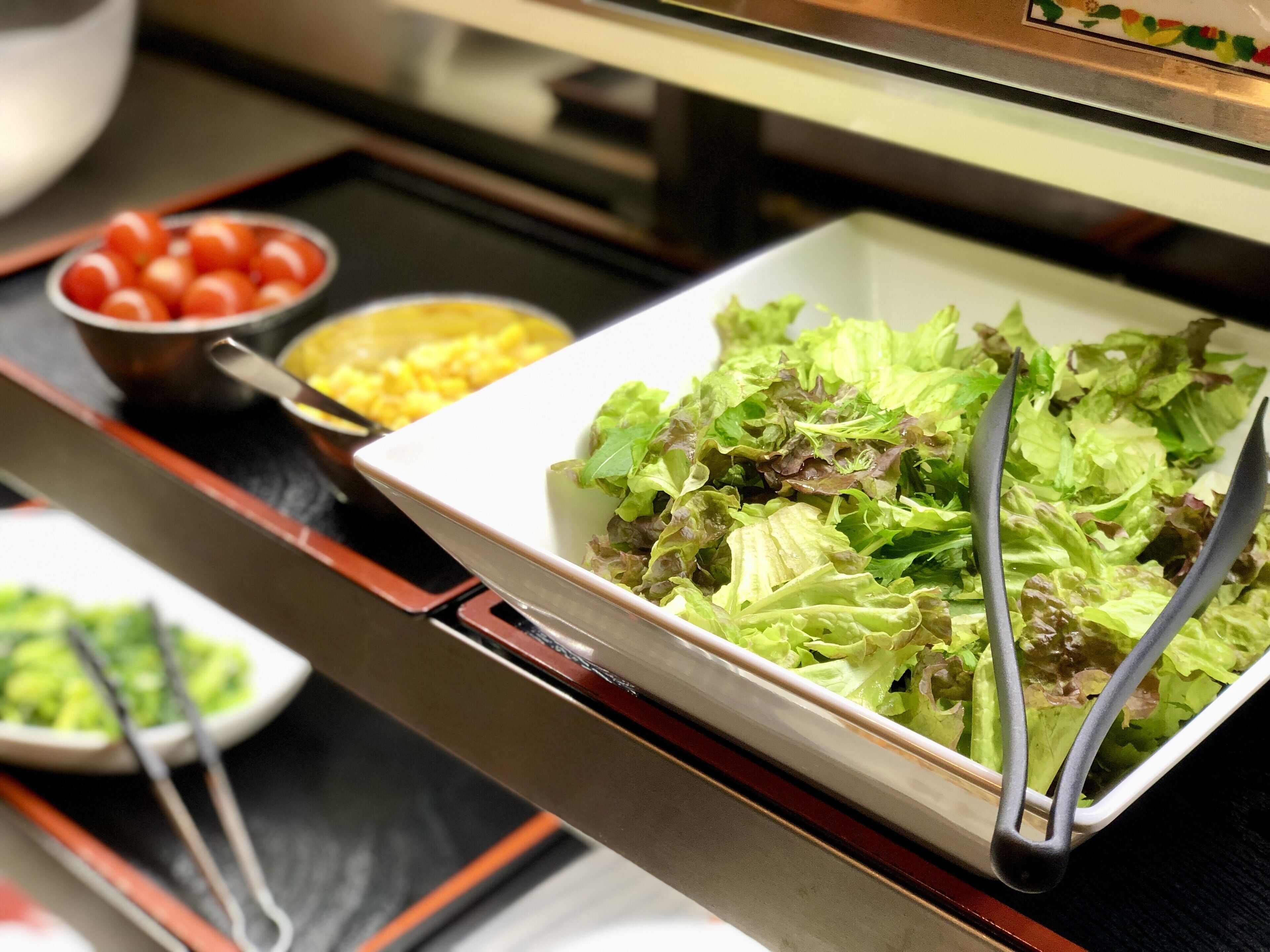 Ein Buffet mit verschiedenen Speisen, darunter eine Salatschüssel, eine Schale mit Cocktailtomaten und eine Schale mit Mais.