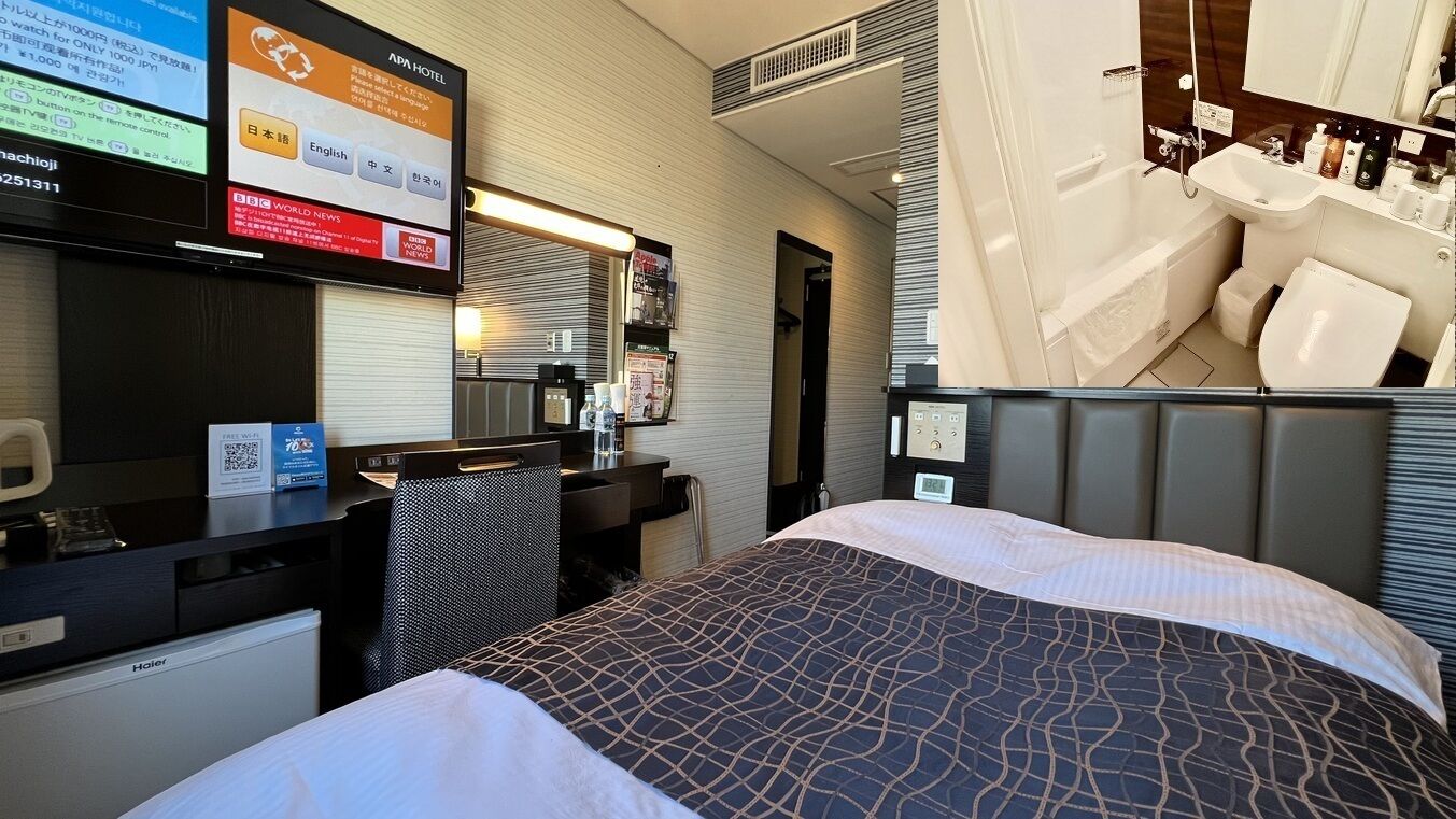 A hotel room with a bed, desk, chair, and a bathroom with a sink and toilet.