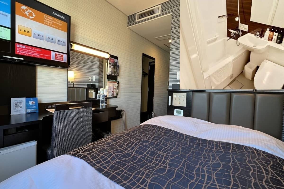 A hotel room with a bed, desk, chair, and a bathroom with a sink and toilet.