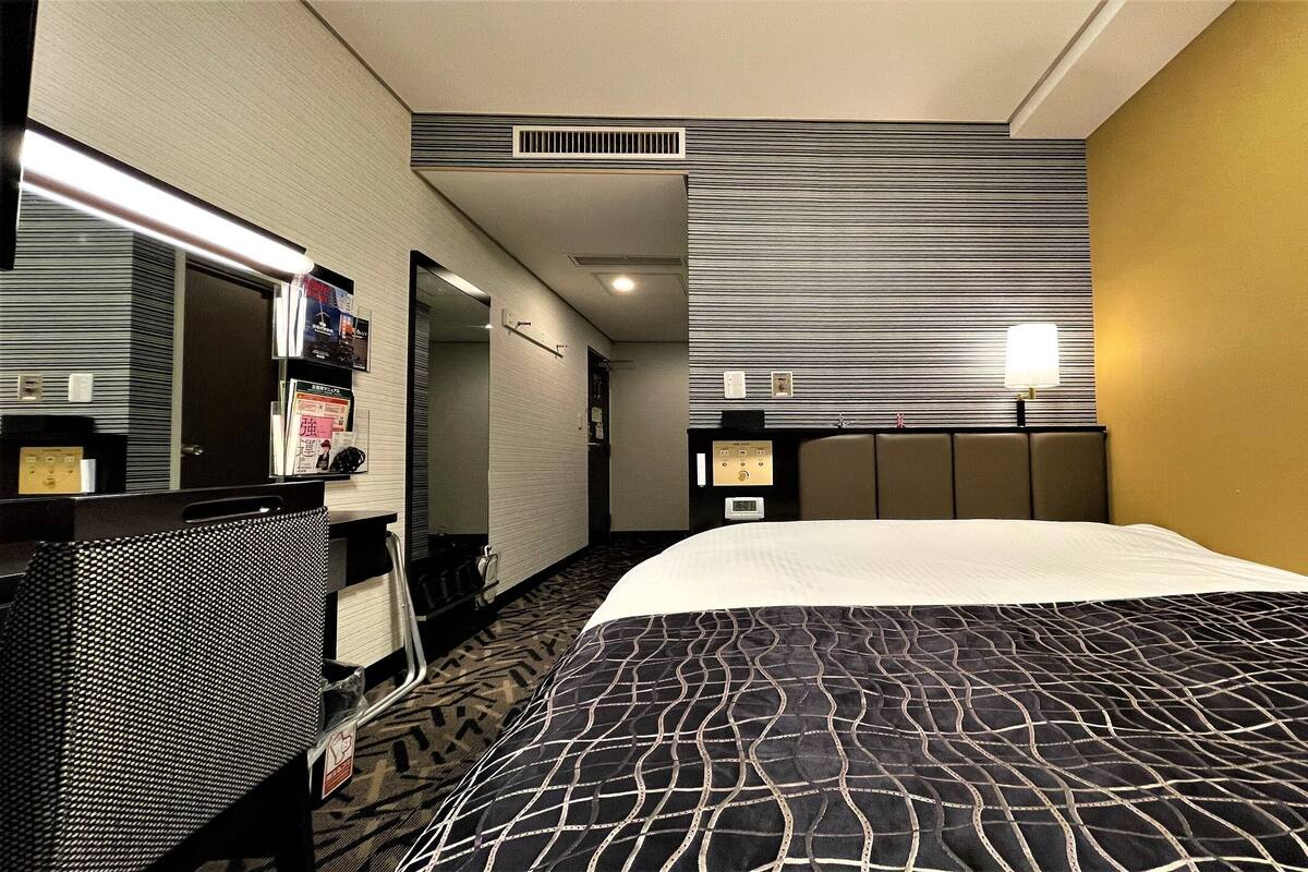 A hotel room with a bed, a desk, a mirror, a wall-mounted TV, and a window.