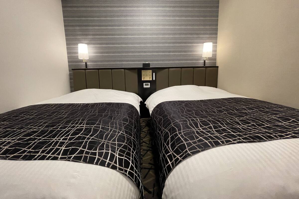 A hotel room with two beds, a striped headboard, and two wall-mounted lights.