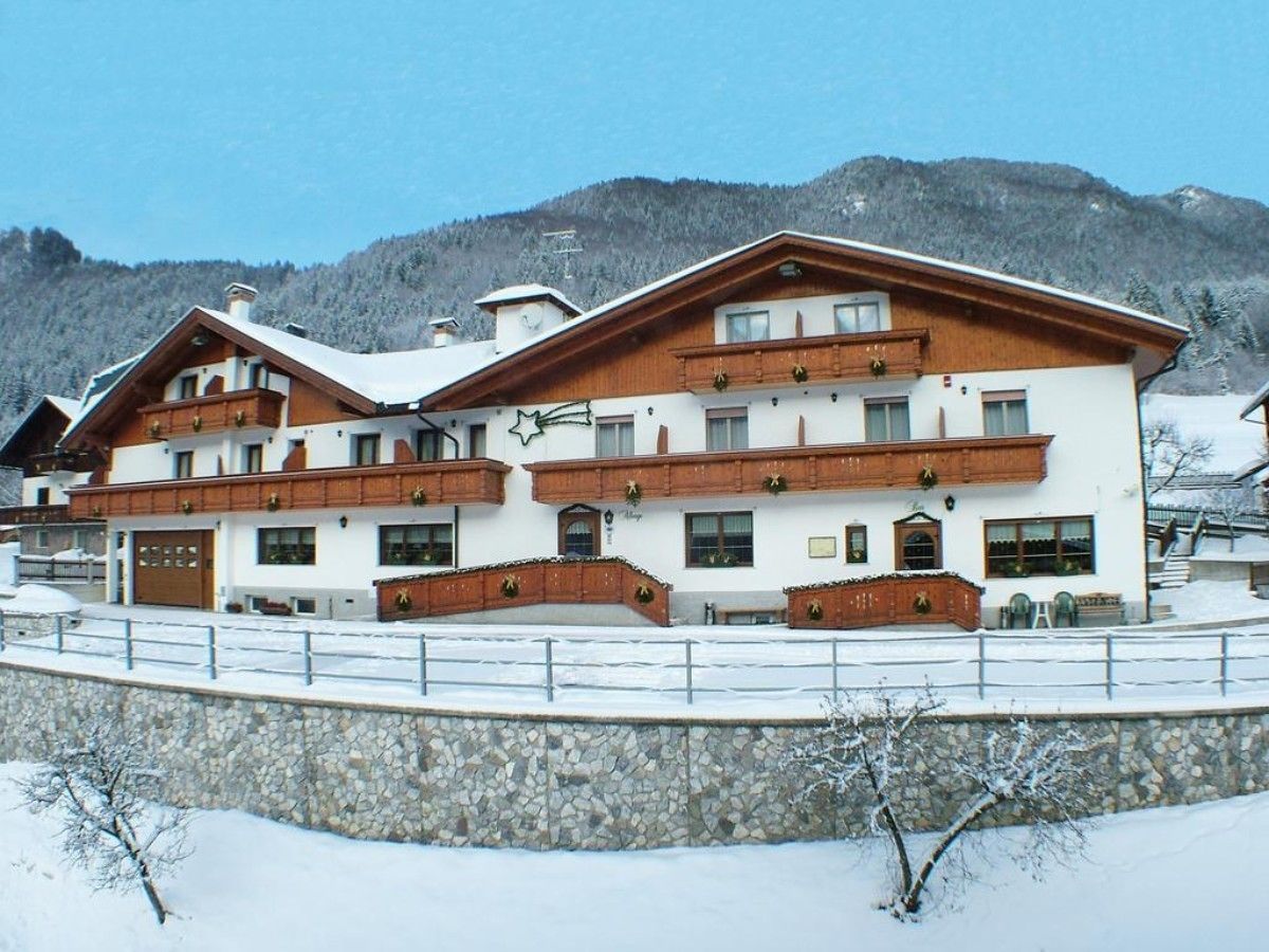 Ein mehrstöckiges Hotel mit einer Steinmauer, hölzernen Balkonen und einer Bergkulisse.