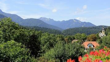 Eine gebirgige Landschaft mit einem Haus mit rotem Dach, umgeben von dichtem Grün und Bäumen.