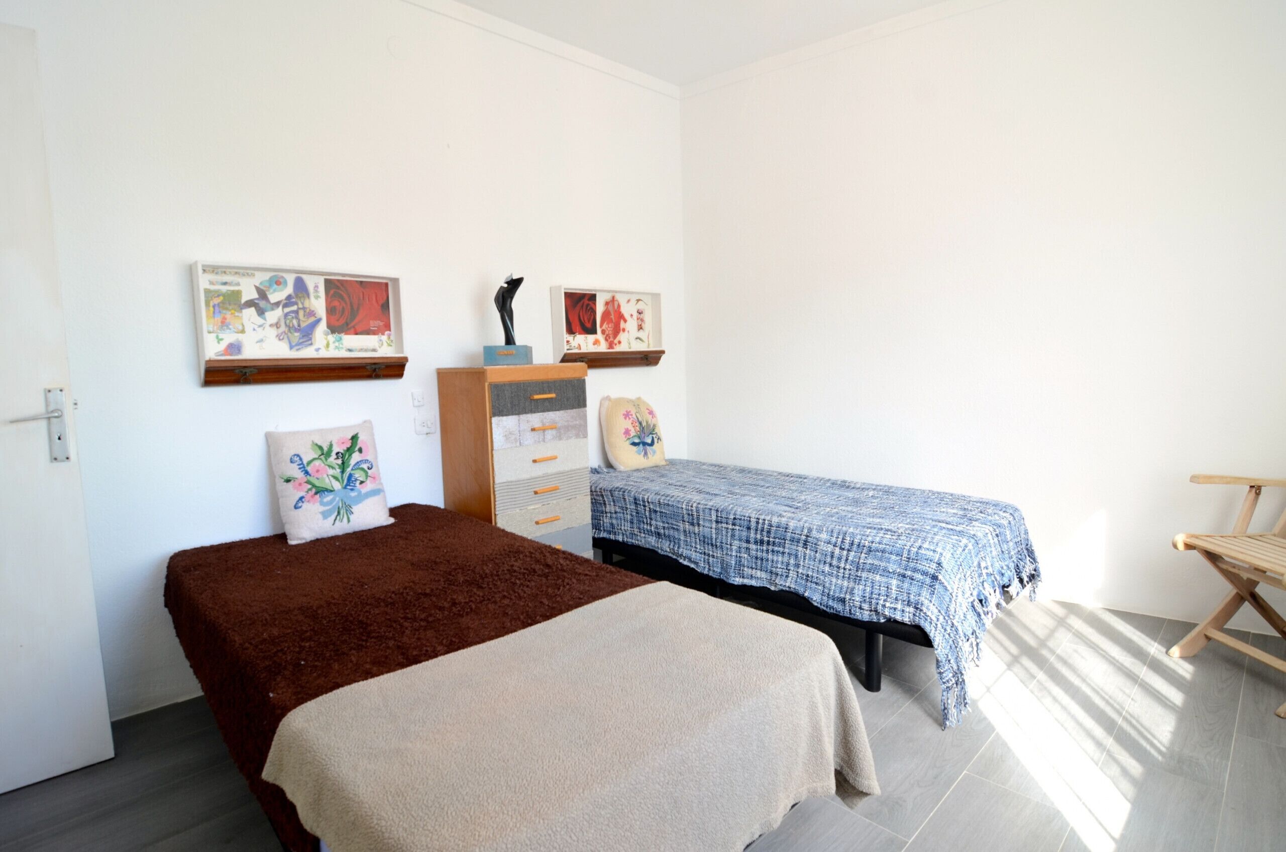 A bedroom with two beds, a dresser, and artwork on the walls.