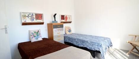 A bedroom with two beds, a dresser, and artwork on the walls.