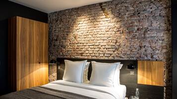 A modern bedroom with a stone wall, a wooden wardrobe, a bed with white linens, and a bedside table with a bottle.