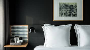A neatly made bed with white linens, a framed artwork above it, and a bedside table with a kettle and cups.