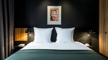 A neatly made bed with white linens, two bedside tables with lamps, a framed abstract painting above the bed, and a dark wall with a wooden panel on the left.