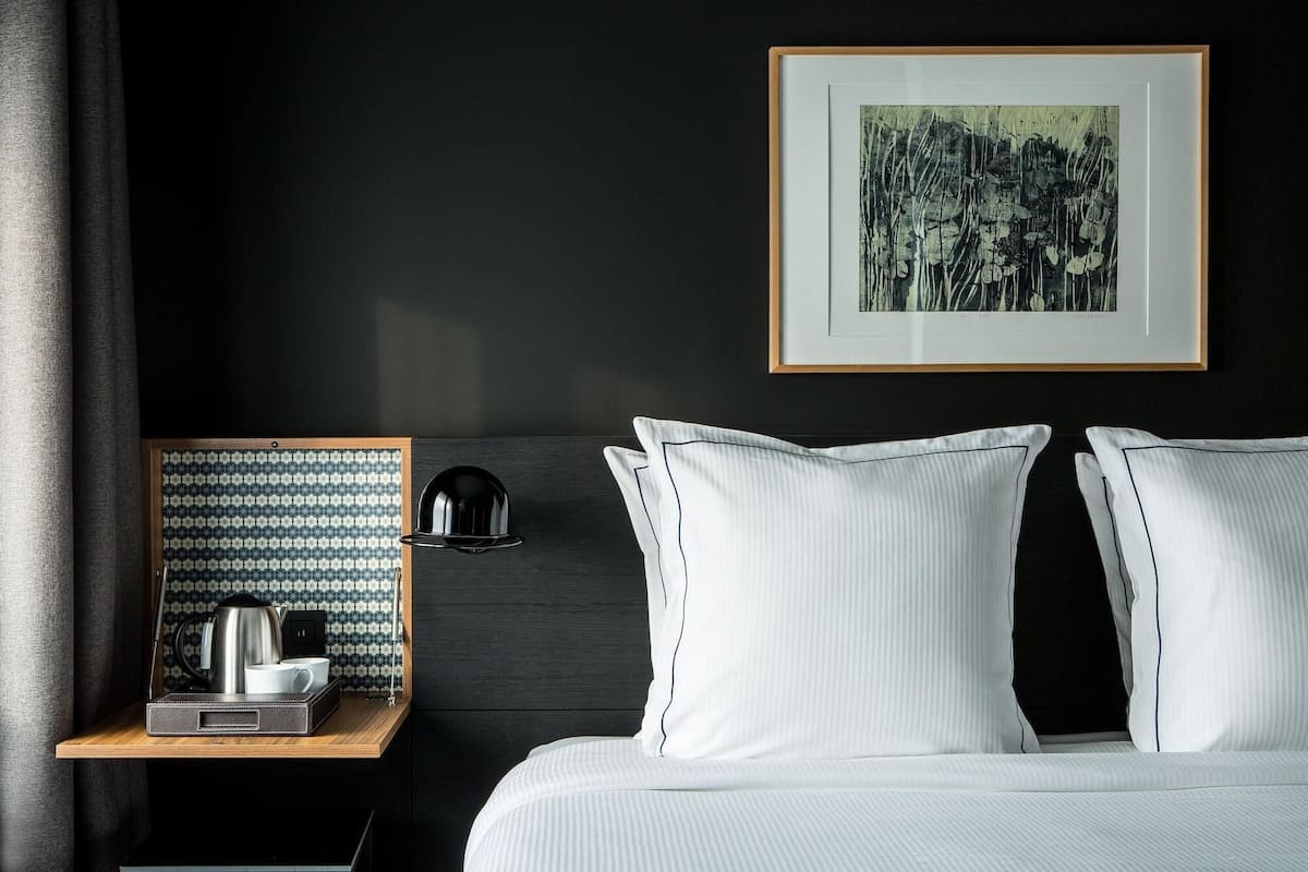 Ein Hotelzimmer mit Bett, Nachttisch, gerahmtem Bild und Wandlampe.