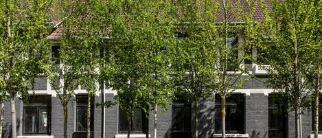 A modern building with a brick facade, multiple windows, and a tree-lined front.