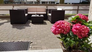 An outdoor seating area with wicker furniture and a potted plant of pink flowers. - Hotel Post (Kelkheim)