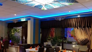 A restaurant with tables set for dining, a ceiling with a star-like pattern, and a view of the outside through a window. - Hotel Post (Kelkheim)