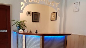 A reception desk with a blue backlight, framed pictures on the wall, and a potted plant. - Hotel Post (Kelkheim)