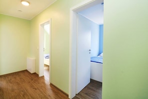 A hallway with a white door leading to a bedroom with a bed and a blue wall.