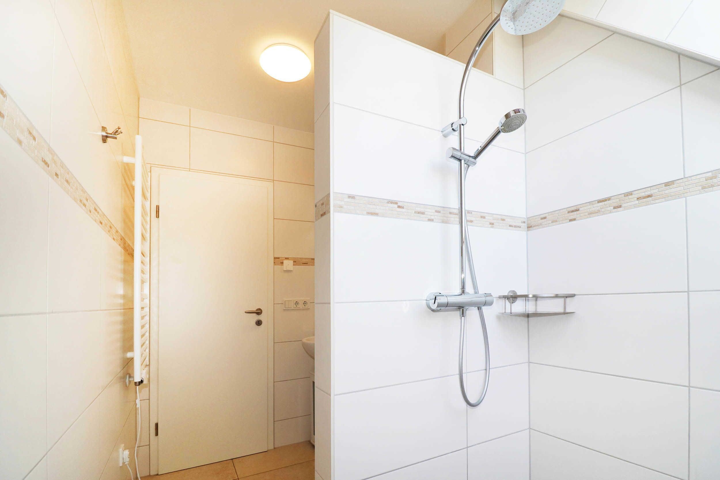A modern bathroom with a shower, a toilet, and a door leading to another room.
